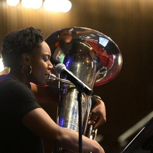 A young woman in a black shirt plays the tuba in a darkened room